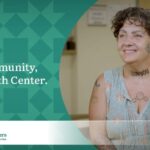 Woman with short curly brown hair, covered in tattoos and wearing a sleeveless floral top promotes the My Community, My Health Center campaign for the Community Health Centers of Benton & Linn Counties (CHC).